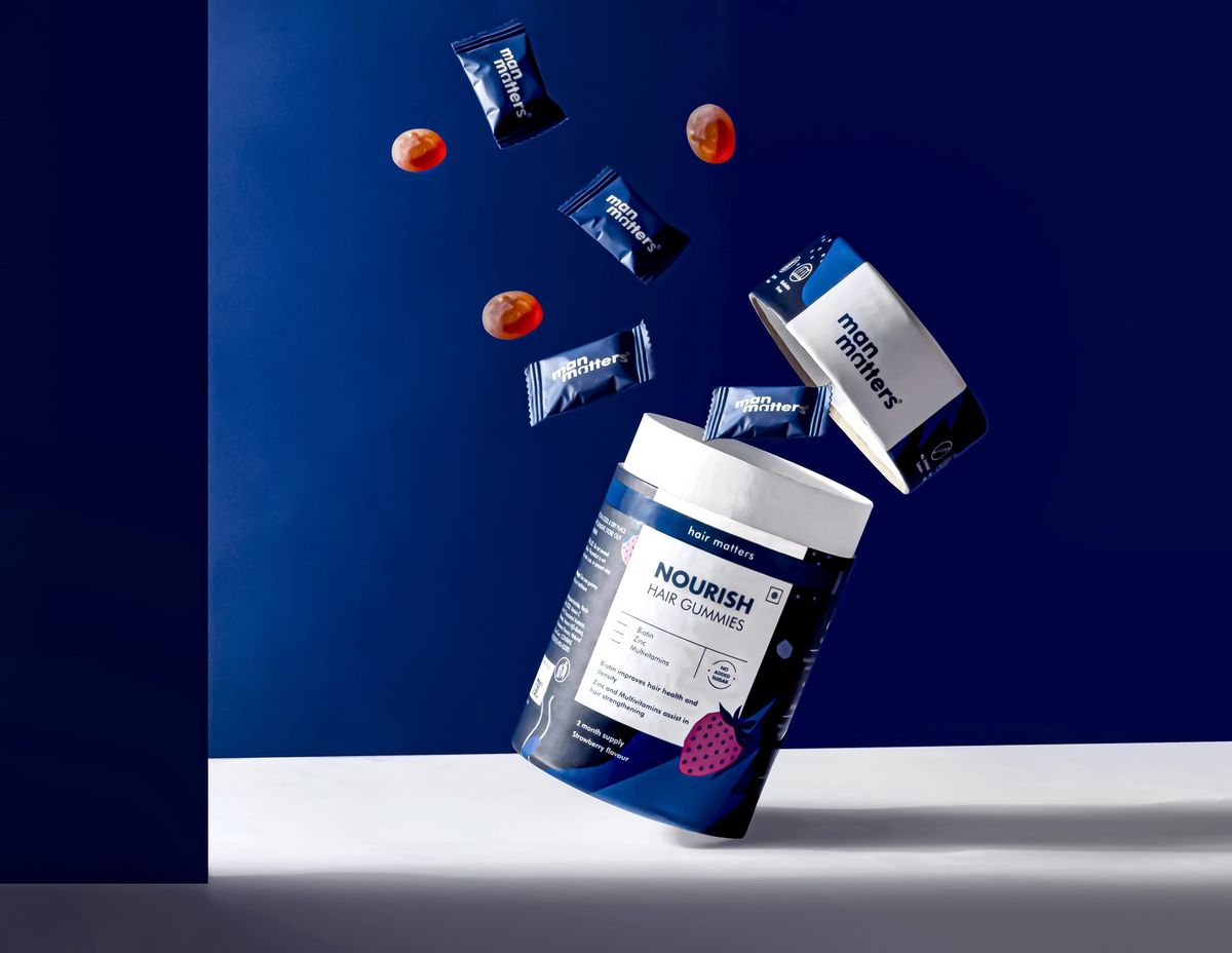 Supplement product photography, hair gummies jar and sachets falling on a deep blue set
